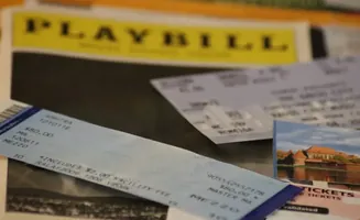 A Playbill and tickets are on a table, with a postcard of a castle in the background.