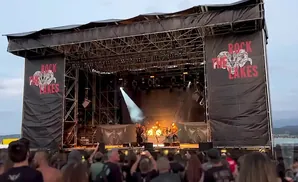 Rock band performing on stage at Rock the Lakes festival, with a crowd in the foreground.