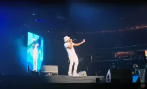A rapper in white performs on stage, holding a microphone and wearing a bucket hat.