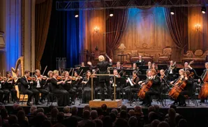 An orchestra performs on stage with a conductor.