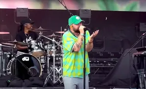 A drummer and a singer perform on a stage, with the drummer on the left and the singer in the center.