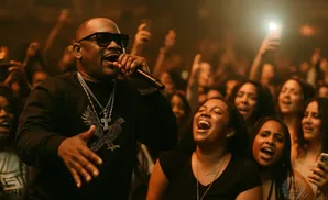 A rapper in sunglasses and a jeweled pendant performs for a lively, cheering crowd at a concert.