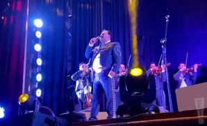 A mariachi singer performs on stage with a band playing violins.