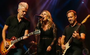 A band performs live on stage, with a male guitarist on the left, a female singer in the center, and a male guitarist on the right.