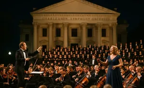 A conductor leads a symphony orchestra and choir in front of a grand building at night.
