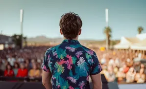 Man in a floral shirt facing a large crowd at an outdoor concert or event.