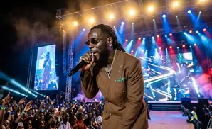 Rapper Burna Boy performs on stage at a concert with a large crowd and stage lights.