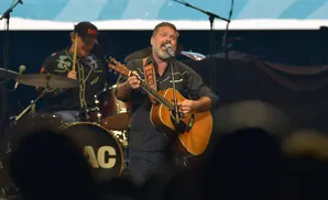 A man with a beard sings and plays an acoustic guitar on stage.