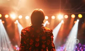 Back view of a person in a vibrant, embroidered jacket on a stage with bright lights.