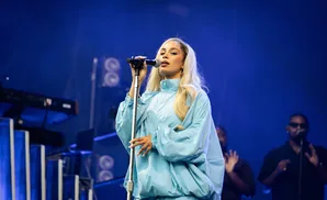 Singer on stage in a blue tracksuit, holding a microphone with a blue background.