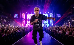 Rapper on stage with fans holding up phone lights in a concert hall.