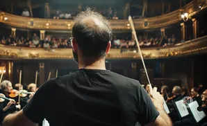 Conductor leading an orchestra in a grand theater, audience in the background.