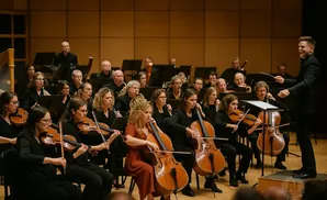 Conductor leads an orchestra of string and woodwind musicians playing during a performance.
