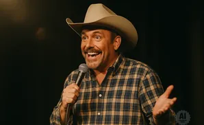 A man in a cowboy hat and plaid shirt holds a microphone and gestures with his hand.