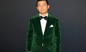 Man in green velvet suit with black bow tie stands against a dark background.