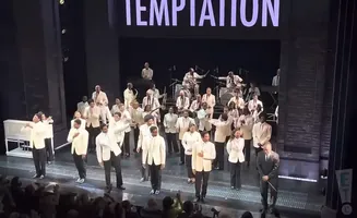 A large ensemble in cream suits performs on stage with 