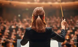 Conductor with baton leading orchestra in a concert hall.
