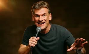 A man with a wide smile and holding a microphone gestures with his hand.
