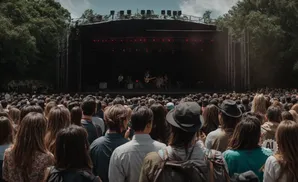 Crowd at an outdoor concert, facing a stage with musicians playing under red lights.