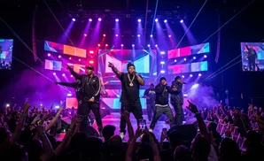 Rappers perform on a brightly lit stage in front of a cheering crowd.