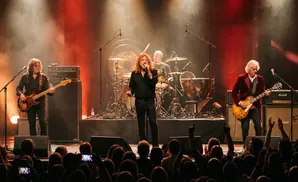 A rock band performs on stage with red lighting and smoke.