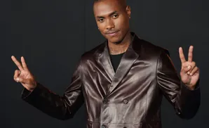 A man in a brown leather suit flashes a peace sign with each hand.