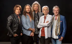 Five men stand against a black backdrop, some with arms crossed.