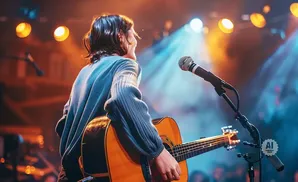 A person plays an acoustic guitar on stage with stage lights and a microphone.