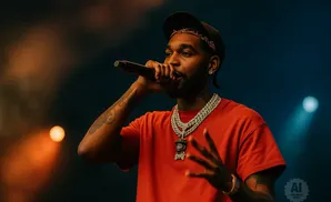 A rapper in a red shirt and gold chains performs on stage.