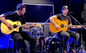 Two men playing acoustic guitars and singing into microphones on a stage.