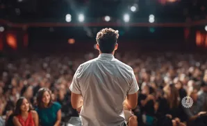 Man in a white shirt speaking to a large, blurred audience from a stage.