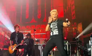 Singer Billy Idol performs on stage with a guitarist and bandmates.
