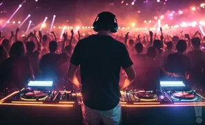 DJ in headphones playing music to a cheering crowd at a concert, illuminated by stage lights.