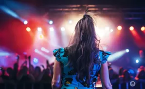 Woman in a blue dress facing a crowd with stage lights in the background.