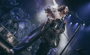 A performer plays a cello on stage with dramatic lighting.