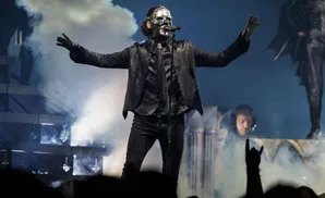 A singer in a skull mask performs on stage with smoke and lights.