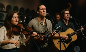 A band plays music; a woman plays violin, a man plays mandolin, and another man plays guitar.
