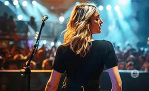 A female singer performs on stage in front of a cheering crowd, with stage lights illuminating the scene.