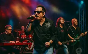 A band performs on stage with a lead singer in sunglasses holding a microphone.