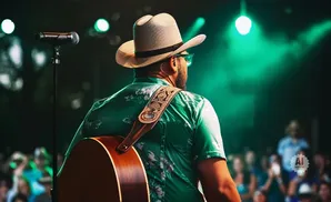Man in a cowboy hat and green floral shirt plays guitar on stage with green lights.