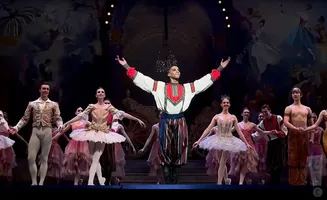 Ballet dancers in elaborate costumes perform on stage.