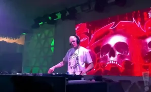 DJ with headphones playing music on turntables, with a large LED screen displaying flaming skulls in the background.