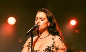 Singer performs into a microphone on stage, bathed in warm, red stage lights.