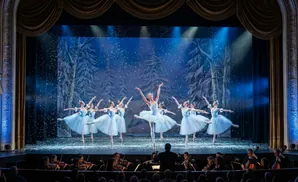 Ballet dancers perform on stage with an orchestra playing in the pit below.
