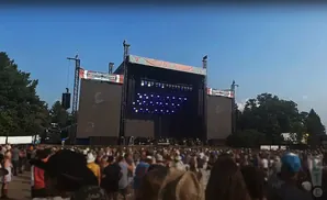 Outdoor concert stage with large screens and a crowd of people. 