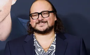 A man with glasses, a beard, and long hair smiles.