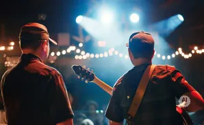 Musicians with caps play guitar on a stage lit by bright spotlights and string lights.