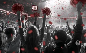 Crowd cheering with red confetti falling, people hold up red pom-poms.