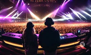 Two DJs at a massive outdoor concert, facing a huge crowd illuminated by purple and yellow stage lights.