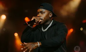 Rapper DaBaby performs onstage, wearing a black jacket, chain, and cap.